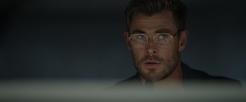 Movie still from “Spiderhead” (2022), directed by Joseph Kosinski – A person wearing a suit and glasses; Close Up shot, Over the shoulder angle