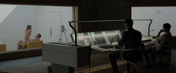 Movie still from “Spiderhead” (2022), directed by Joseph Kosinski – A person sitting at a desk with a laptop; Wide shot, Low angle