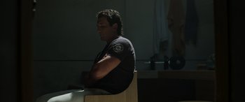 Movie still from “Spiderhead” (2022), directed by Joseph Kosinski – A man sitting on a chair with his arms crossed; Medium shot, Low angle