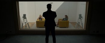 Movie still from “Spiderhead” (2022), directed by Joseph Kosinski – A man standing in front of two women sitting on yellow chairs; Wide shot, Over the shoulder angle