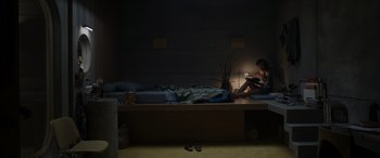 Movie still from “Spiderhead” (2022), directed by Joseph Kosinski – A person sitting on a bed in a dark room; Extreme Wide shot, High angle