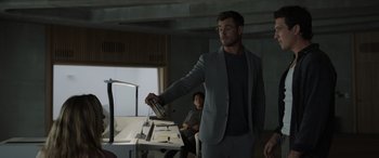 Movie still from “Spiderhead” (2022), directed by Joseph Kosinski – A man in a gray suit is holding a bottle; Medium shot, Over the shoulder angle