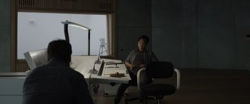 Movie still from “Spiderhead” (2022), directed by Joseph Kosinski – A man sitting at a desk in front of a window; Medium shot, Over the shoulder angle