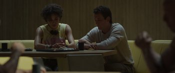 Movie still from “Spiderhead” (2022), directed by Joseph Kosinski – A man and a woman sitting at a table; Medium shot, Low angle