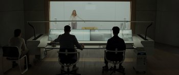 Movie still from “Spiderhead” (2022), directed by Joseph Kosinski – Two men sitting in front of a woman in a white room; Wide shot, Low angle
