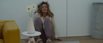 Movie still from “Spiderhead” (2022), directed by Joseph Kosinski – A woman sitting on the ground with her hands on her knees; Medium shot, High angle