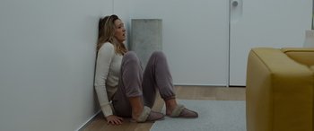 Movie still from “Spiderhead” (2022), directed by Joseph Kosinski – A woman sitting on the ground in a room; Wide shot, High angle