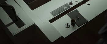 Movie still from “Spiderhead” (2022), directed by Joseph Kosinski – A computer desk with a cup of coffee and a keyboard; Wide shot, Overhead angle