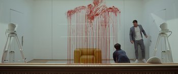Movie still from “Spiderhead” (2022), directed by Joseph Kosinski – A man looking at a chair with blood coming out of it; Wide shot, Low angle