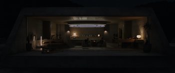 Movie still from “Spiderhead” (2022), directed by Joseph Kosinski – A man sitting on a couch in a living room at night; Extreme Wide shot, Low angle