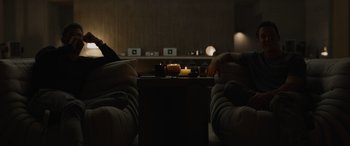 Movie still from “Spiderhead” (2022), directed by Joseph Kosinski – Two people sitting in a dark room with a candle; Wide shot, High angle