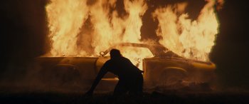 Movie still from “Spiderhead” (2022), directed by Joseph Kosinski – A man standing in front of a burning car; Wide shot, Low angle