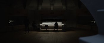 Movie still from “Spiderhead” (2022), directed by Joseph Kosinski – Two people sitting on chairs in a dark room; Extreme Wide shot, Low angle