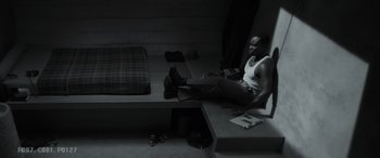 Movie still from “Spiderhead” (2022), directed by Joseph Kosinski – A black and white photo of a man sitting on a bed; Wide shot, Overhead angle