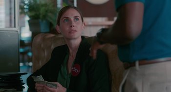 Movie still from “Spin Me Round” (2022), directed by Jeff Baena – A woman sitting on a couch holding a stack of money; Close Up shot, Over the shoulder angle