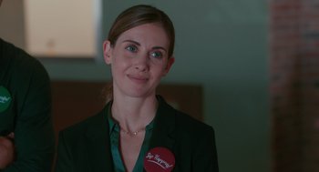 Movie still from “Spin Me Round” (2022), directed by Jeff Baena – A woman wearing a green jacket and a red button; Close Up shot, Over the shoulder angle