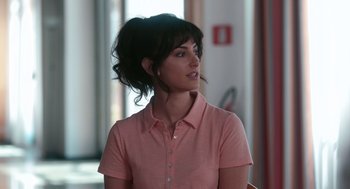 Movie still from “Spin Me Round” (2022), directed by Jeff Baena – A woman in a pink shirt looking to her left; Close Up shot, Over the shoulder angle
