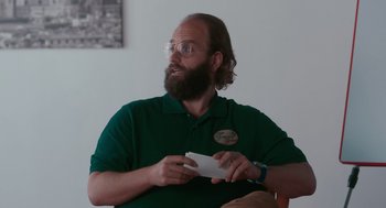 Movie still from “Spin Me Round” (2022), directed by Jeff Baena – A man with a beard is holding a piece of paper in his hand; Close Up shot, Over the shoulder angle