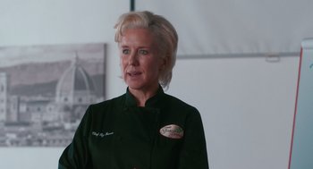 Movie still from “Spin Me Round” (2022), directed by Jeff Baena – A woman with blonde hair wearing a black chef's outfit; Close Up shot, Over the shoulder angle