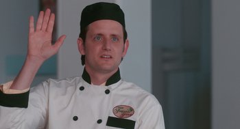 Movie still from “Spin Me Round” (2022), directed by Jeff Baena – A man in a chef's outfit is waving; Close Up shot, Over the shoulder angle