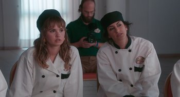 Movie still from “Spin Me Round” (2022), directed by Jeff Baena – Two women in chef's outfits sitting next to each other; Medium shot, Over the shoulder angle