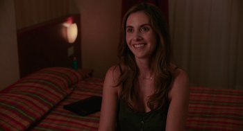 Movie still from “Spin Me Round” (2022), directed by Jeff Baena – A woman sitting on a bed smiling at the camera; Close Up shot, Over the shoulder angle