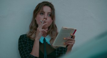 Movie still from “Spin Me Round” (2022), directed by Jeff Baena – A woman smoking a cigarette while holding an open book; Close Up shot, Low angle
