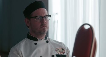 Movie still from “Spin Me Round” (2022), directed by Jeff Baena – A man in a chef's outfit looking at a mirror; Close Up shot, Over the shoulder angle