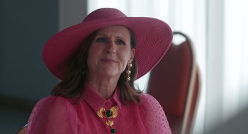 Movie still from “Spin Me Round” (2022), directed by Jeff Baena – A woman wearing a pink hat and a gold necklace; Close Up shot, Over the shoulder angle