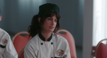 Movie still from “Spin Me Round” (2022), directed by Jeff Baena – A woman in a chef's outfit is sitting in a chair; Close Up shot, Over the shoulder angle