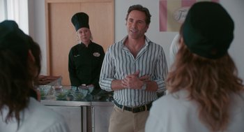 Movie still from “Spin Me Round” (2022), directed by Jeff Baena – A man standing in front of a woman in front of a counter; Medium shot, Over the shoulder angle