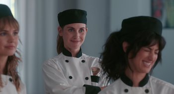 Movie still from “Spin Me Round” (2022), directed by Jeff Baena – A woman in a chef's outfit smiles for the camera; Close Up shot, Over the shoulder angle