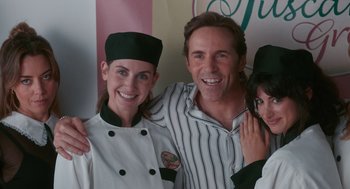 Movie still from “Spin Me Round” (2022), directed by Jeff Baena – A man and two women posing for a picture; Medium shot, Low angle