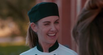 Movie still from “Spin Me Round” (2022), directed by Jeff Baena – A woman in a chef's outfit smiling for the camera; Close Up shot, Over the shoulder angle