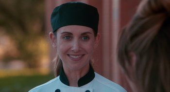 Movie still from “Spin Me Round” (2022), directed by Jeff Baena – A woman in a chef's outfit smiling for the camera; Close Up shot, Over the shoulder angle
