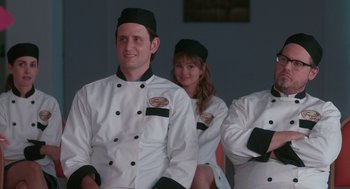 Movie still from “Spin Me Round” (2022), directed by Jeff Baena – A group of people in chef's outfits sitting in a row; Medium shot, Over the shoulder angle