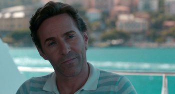 Movie still from “Spin Me Round” (2022), directed by Jeff Baena – A person sitting in front of a body of water; Close Up shot, Over the shoulder angle