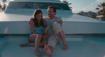 Movie still from “Spin Me Round” (2022), directed by Jeff Baena – A man and a woman sitting on the back of a boat; Medium shot, Low angle