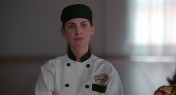 Movie still from “Spin Me Round” (2022), directed by Jeff Baena – A woman in a chef's outfit posing for a picture; Close Up shot, Over the shoulder angle