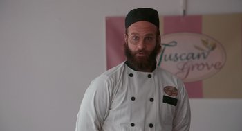 Movie still from “Spin Me Round” (2022), directed by Jeff Baena – A man with a beard wearing a chef's outfit; Medium shot, Low angle