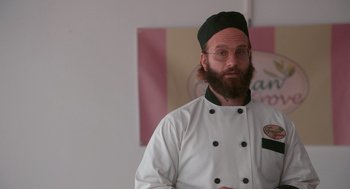 Movie still from “Spin Me Round” (2022), directed by Jeff Baena – A man with a beard wearing a chef's outfit; Medium shot, Over the shoulder angle