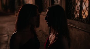 Movie still from “Spin Me Round” (2022), directed by Jeff Baena – Two women standing next to each other in a dark room; Close Up shot, Over the shoulder angle
