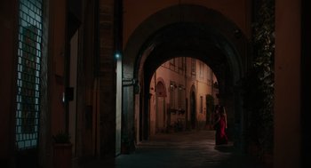 Movie still from “Spin Me Round” (2022), directed by Jeff Baena – A woman in a red dress walking down a street; Extreme Wide shot, Over the shoulder angle