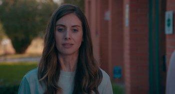 Movie still from “Spin Me Round” (2022), directed by Jeff Baena – A woman with long brown hair standing in front of a brick building; Close Up shot, Over the shoulder angle