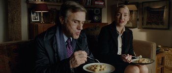 Movie still from “Carnage” (2011), directed by Roman Polanski – A man and a woman sitting at a table with a plate of food; Medium shot, Over the shoulder angle