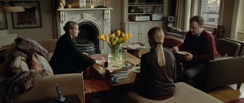 Movie still from “Carnage” (2011), directed by Roman Polanski – Two women sitting at a table in front of a fireplace; Medium shot, Over the shoulder angle