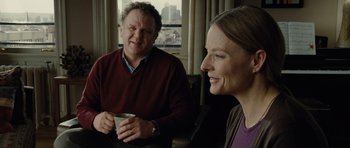 Movie still from “Carnage” (2011), directed by Roman Polanski – A man and a woman sitting next to each other holding a cup; Medium shot, Over the shoulder angle