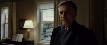 Movie still from “Carnage” (2011), directed by Roman Polanski – A man standing in front of a window in a room; Close Up shot, Over the shoulder angle