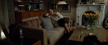 Movie still from “Carnage” (2011), directed by Roman Polanski – A woman sitting on top of a couch in a living room; Wide shot, High angle