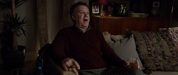 Movie still from “Carnage” (2011), directed by Roman Polanski – An older man sitting on a couch with his mouth wide open; Medium shot, Over the shoulder angle